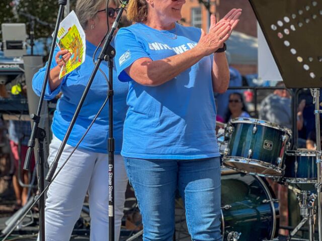 Lori and other staff members are on a stage, congratulating the winners of the chili cook-off. They are likely expressing their appreciation and recognition for the individuals or teams who prepared the best chili dishes in the competition.