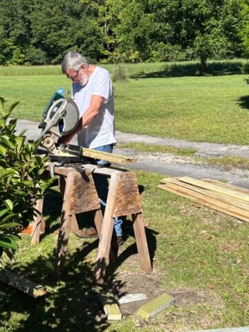 An elderly individual is using a circular saw to cut wooden planks.