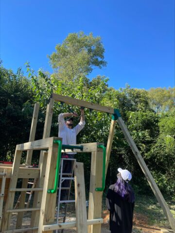 Two people are working together to assemble and set up a swing set for children to play on.